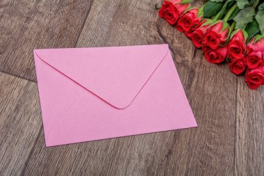 Pembe zarf ve gül ahşap arka plan üzerinde