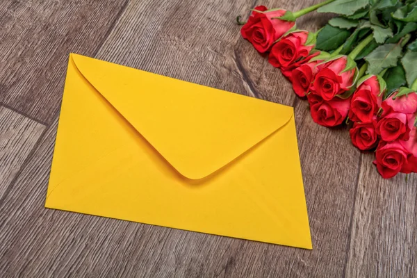 Envelope amarelo e rosas em um fundo de madeira — Fotografia de Stock