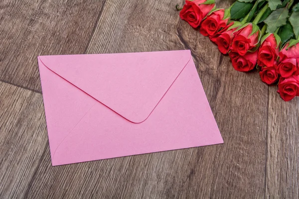Envelope rosa e rosas em um fundo de madeira — Fotografia de Stock