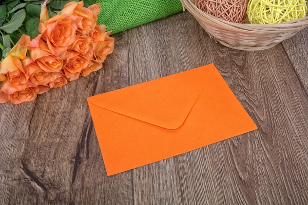 Envelope laranja e rosas em um fundo de madeira — Fotografia de Stock