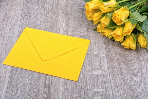 Gelber Umschlag und Rosen auf einem hölzernen Hintergrund — Stockfoto