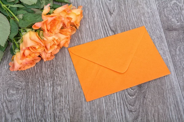Orange kuvert och rosor på en trä bakgrund — Stockfoto