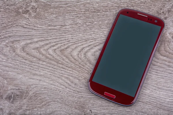 Telefone celular vermelho em um fundo de madeira — Fotografia de Stock