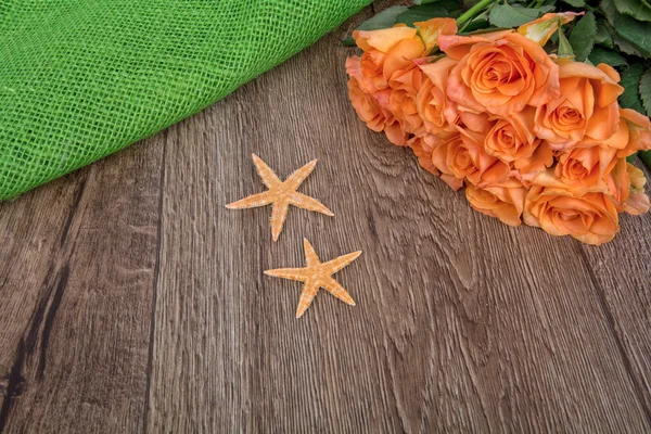 Estrellas de mar y rosas anaranjadas sobre fondo de madera — Foto de Stock