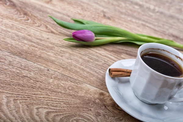 A cup of coffee with cinnamon and purple tulips