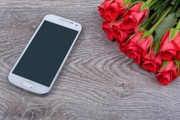 Белый мобильный телефон и розы на деревянном фоне — стоковое фото