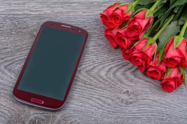 Teléfono móvil rojo y rosas sobre fondo de madera — Foto de Stock