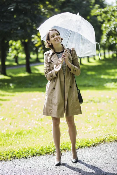 Donna a cappotto beige con ombrello sotto la luce del sole — Foto Stock