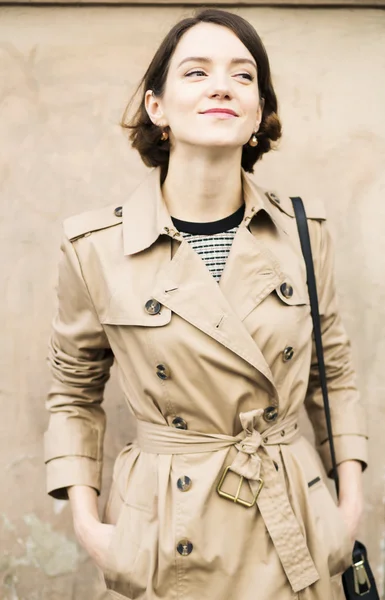 Kvinna på beige kappa med handväska leende smyga — Stockfoto