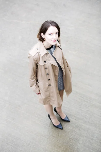 Frau im lockeren beigen Mantel auf grauem Platz — Stockfoto