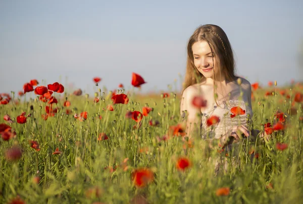 Frau im weißen Kleid spaziert zwischen Mohn — Stockfoto