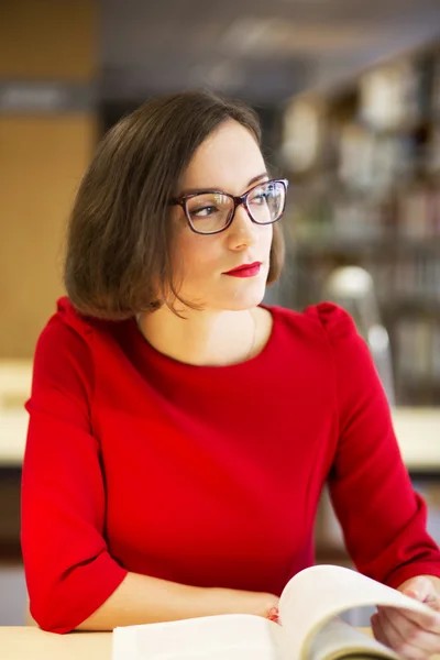 Kvinna med glasögon i biblioteket med bok — Stockfoto
