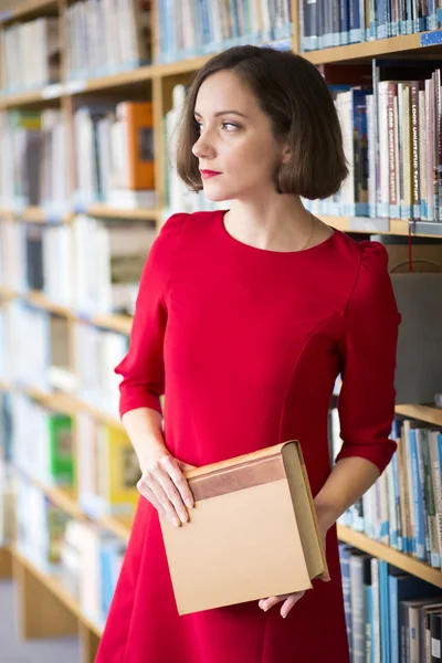 Mulher na biblioteca com o livro olha para o lado — Fotografia de Stock