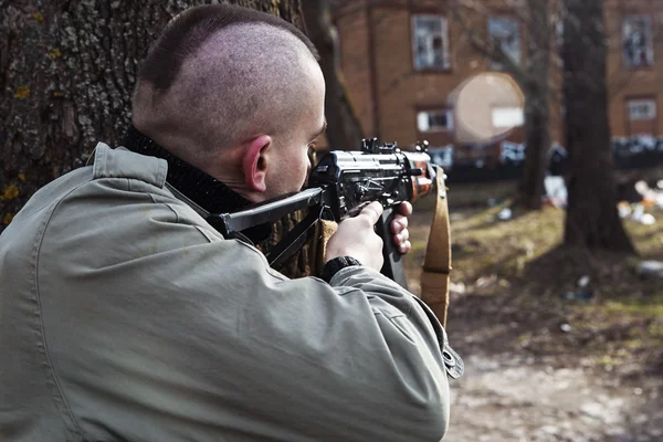 スキンヘッド男性銃で木の後ろの誰かに恐れがあります。 ストック写真