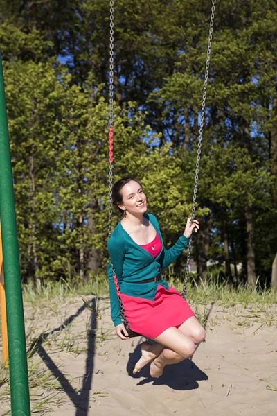 Smiling girl swings on the sunny beach — Stock fotografie