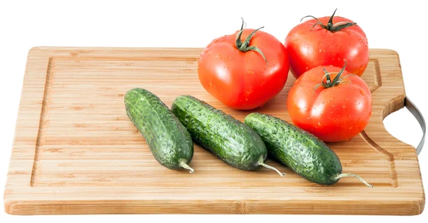 Pepinos e tomates em uma prancha de corte — Fotografia de Stock