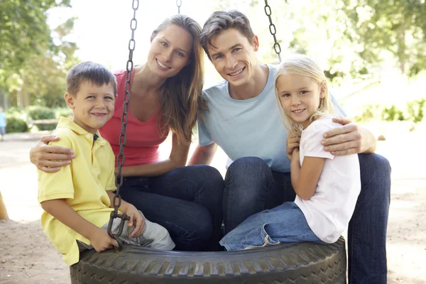Семья, сидящая на качелях в шинах детской площадки — стоковое фото