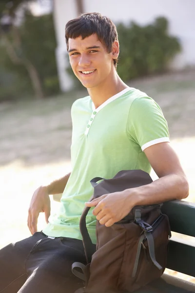 Estudante universitário sentado no banco com mochila — Fotografia de Stock