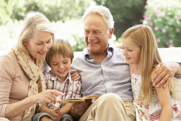 Бабушка с дедушкой читают внукам на диване — стоковое фото