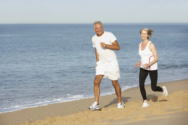 Pareja mayor corriendo a lo largo de la playa — Foto de Stock