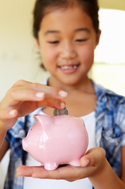 Young girl putting money in piggybank clipart