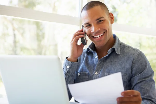 Uomo Talkng sul telefono utilizzando il computer portatile a casa — Foto Stock