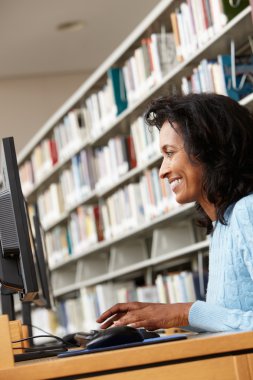 Woman working on computer in library clipart