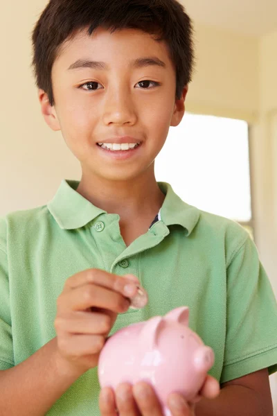 Мальчик кладет деньги в копилку — стоковое фото