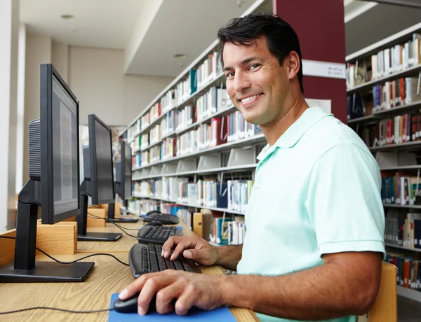 Mężczyzna pracujący na komputerze w bibliotece — Zdjęcie stockowe