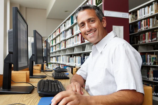 Чоловік працює на комп'ютері в бібліотеці — стокове фото
