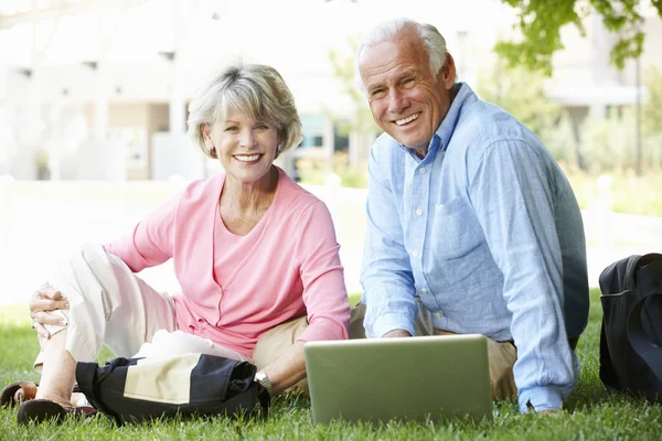 Äldre par med laptop i park — Stockfoto