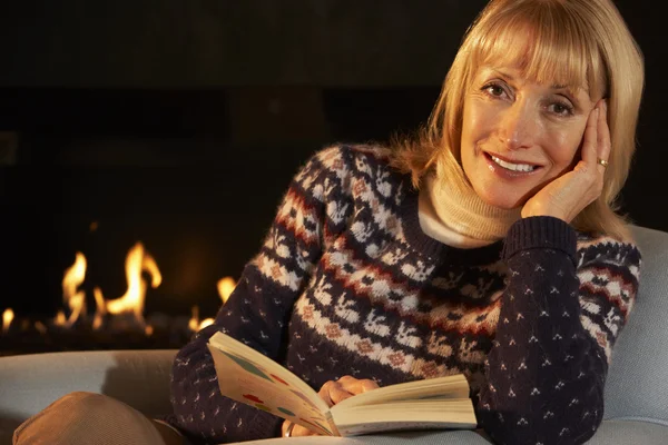 Rijpe vrouw lezen bij het haardvuur — Stockfoto