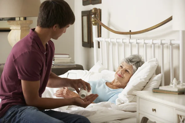 Vnuk dávat lék babička v posteli — Stock fotografie