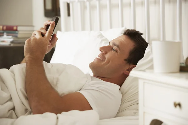 Человек в постели Текст на мобильном телефоне — стоковое фото