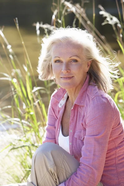 Senior vrouw ontspannen langs kant van Lake — Stockfoto