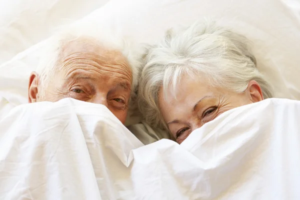 Casal sênior relaxando na cama escondida sob lençóis — Fotografia de Stock