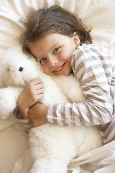 Młoda dziewczyna relaksując się w łóżku z zabawkami — Zdjęcie stockowe