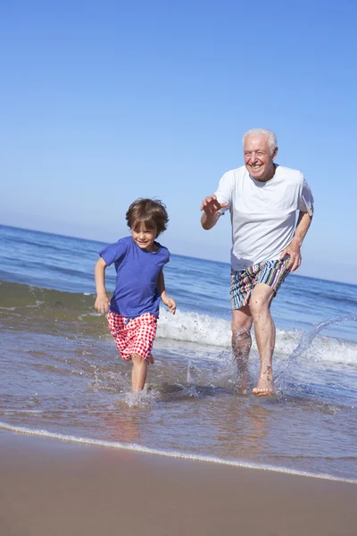 Abuelo persiguiendo nieto a lo largo de la playa —  Fotos de Stock