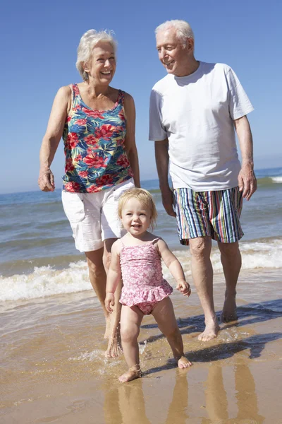 Бабушка с дедушкой и внучка прогуливаются вдоль пляжа — стоковое фото