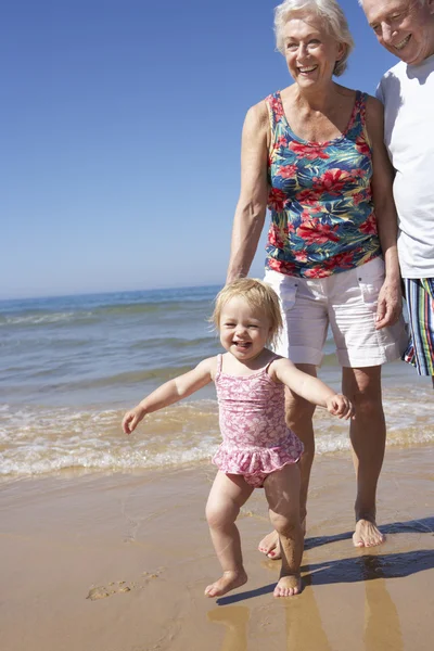 Großeltern und Enkelin laufen am Strand entlang — Stockfoto