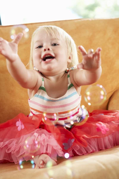 Menina brincando com bolhas no sofá — Fotografia de Stock