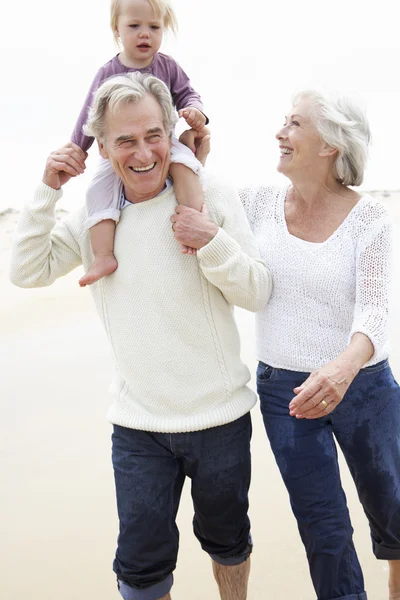 Großeltern und Enkelin laufen am Strand entlang — Stockfoto