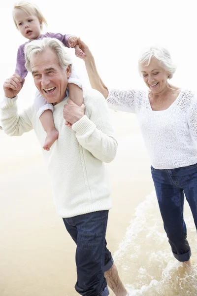 Бабушка с дедушкой и внучка прогуливаются вдоль пляжа — стоковое фото