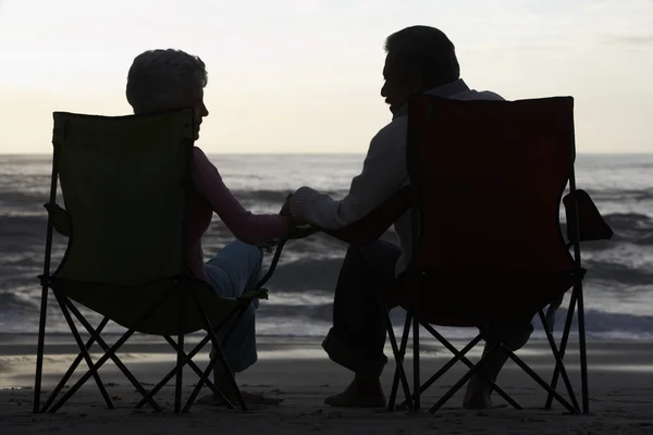 Äldre par sitter på stranden i solstolar — Stockfoto