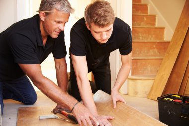 Men laying wood panel flooring in a house clipart