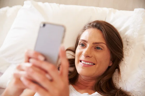 Vrouw met mobiele telefoon in bed — Stockfoto