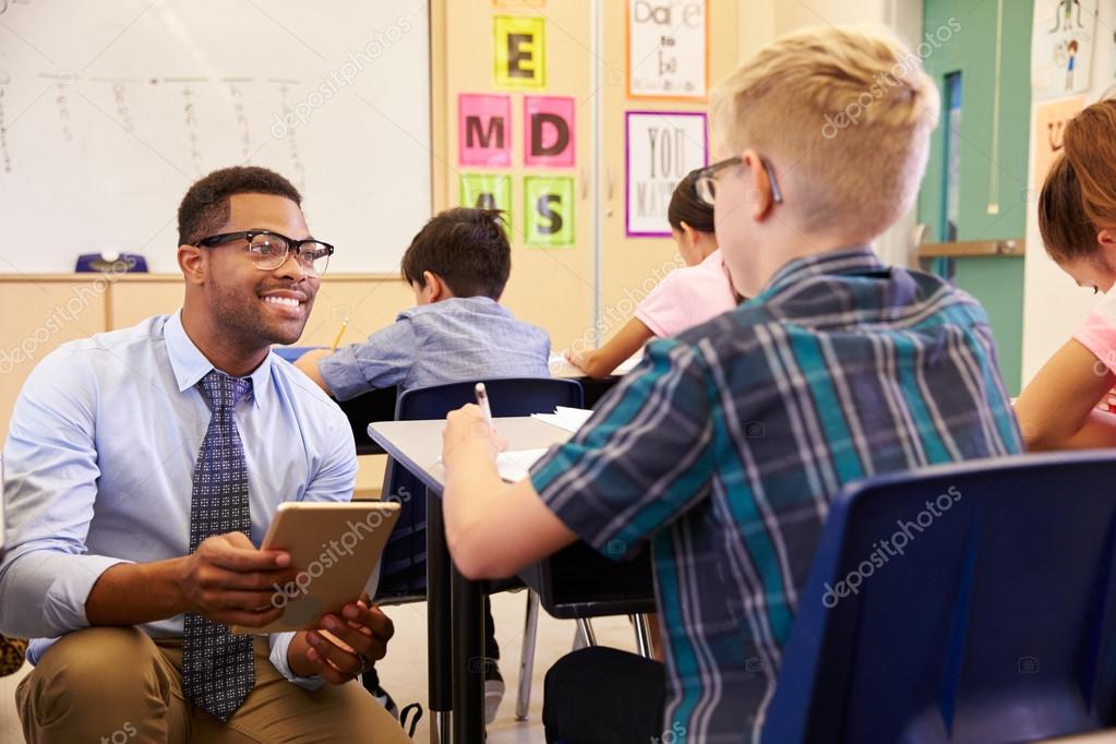 Teacher kneeling beside pupil's desk Stock Photo by ©monkeybusiness
