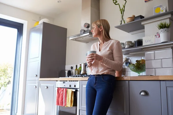 Mulher em pé na cozinha com bebida quente — Fotografia de Stock