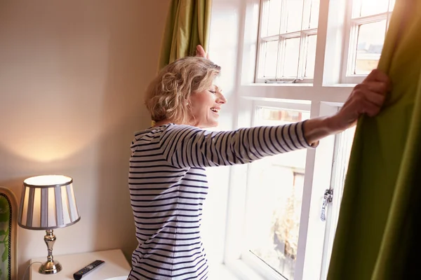 Senior woman opening curtains — Stock Photo, Image