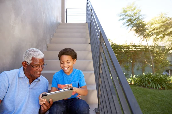 孫と祖父は自宅で屋外でデジタルタブレットを使用してステップに座っています — ストック写真